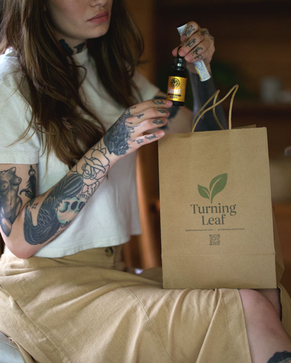 Woman in white shirt with tattooed hands holds Turning Leaf bag and fills with Foundry Nation Indica CBD Oil and other exciting finds