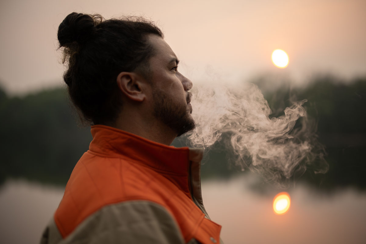 Man blows Smoke Cloud as he looks over sunsetting on the lake.